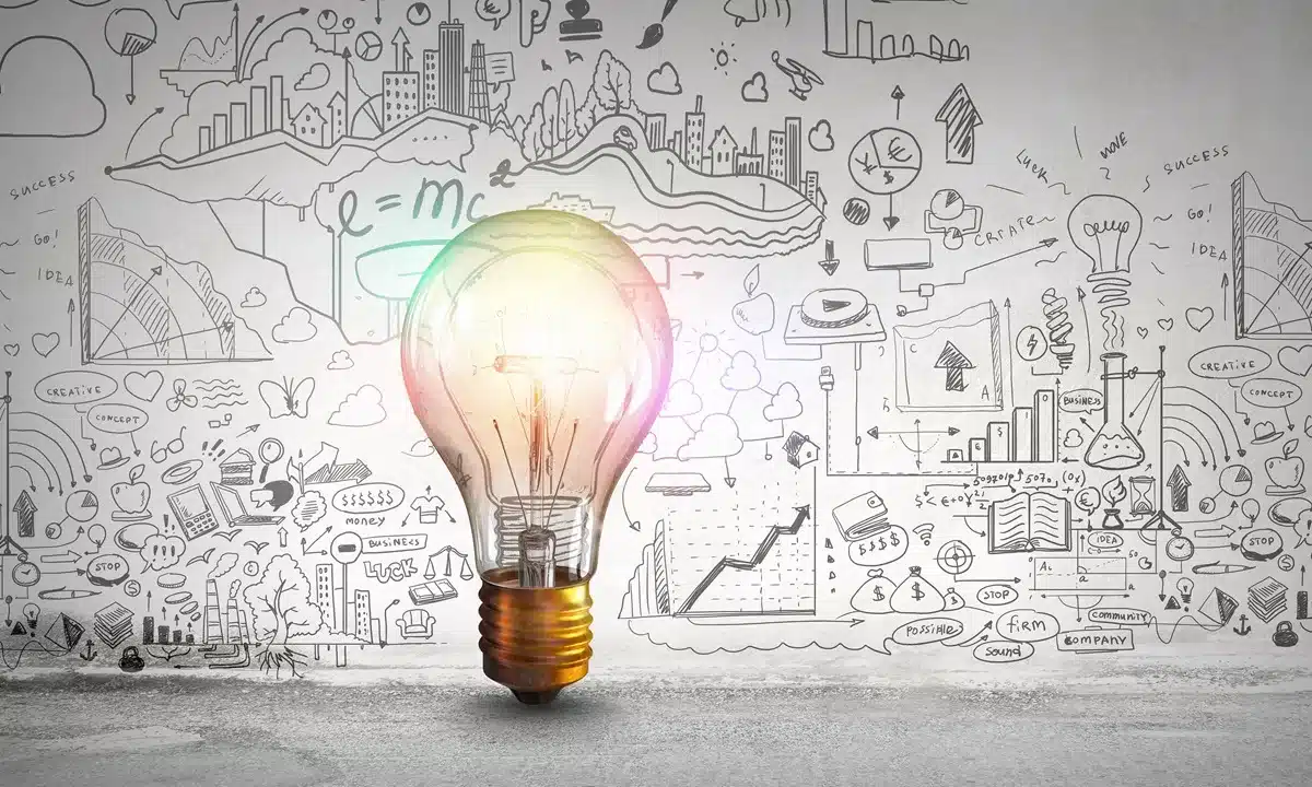 Glowing lightbulb in front of a wall covered with business charts, graphs, and creative sketches, symbolizing discovery, ideas, and structured innovation in game development.