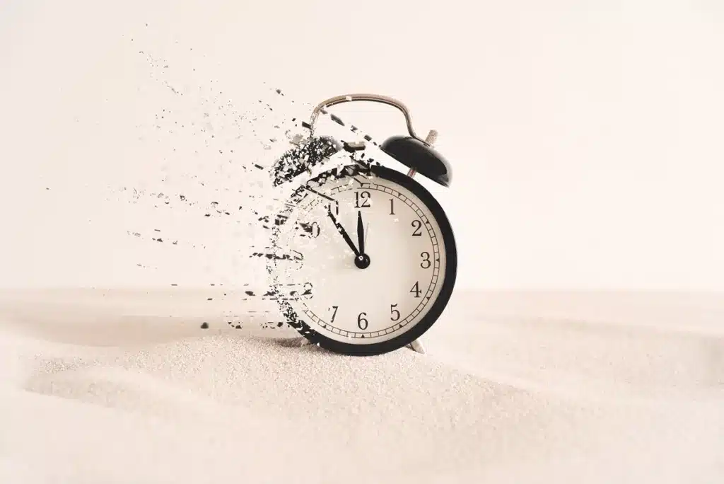 Disintegrating alarm clock in sand, symbolizing the fragility and inaccuracy of time estimation in game development.