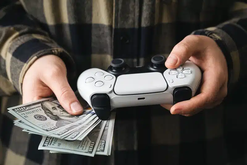 Person holding a video game controller and cash, symbolizing game monetization and revenue strategies in the gaming industry.